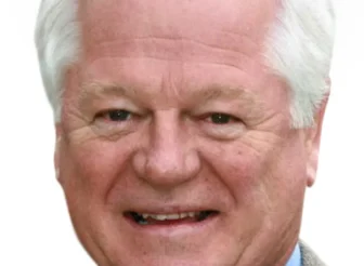 A professional headshot of Brendon Lunney, AWN Deputy Chairman, smiling. He is an older man with white hair, wearing a light blue collared shirt, a reddish-brown tie, and a textured brown jacket, against a plain light background.