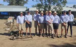 A group of stock agents from the AWN Wimmera Livestock and Property team, wearing hats and work attire, standing outdoors in an agricultural setting with farm buildings in the background at a recent farm clearing sale.